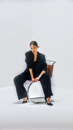 a woman sitting on top of a chair in front of a white wall with her legs crossed