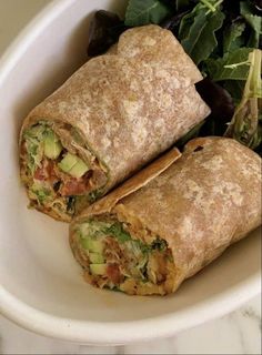 two burritos sitting on top of a white plate next to a green salad