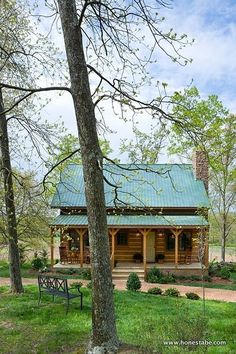 a log cabin sits in the middle of a grassy area with trees and benches around it