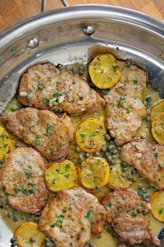 some meat and vegetables are cooking in a pan on the stove top with lemons