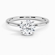 a white gold ring with a round brilliant cut diamond in the center, on a plain surface