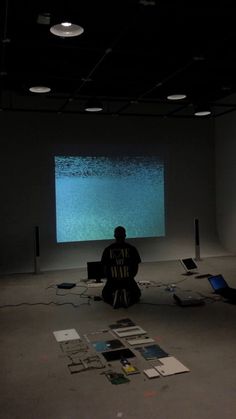 a man sitting on the floor in front of a projector screen and laptop computer