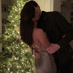 a man and woman kissing in front of a christmas tree