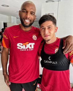 two men standing next to each other wearing red shirts