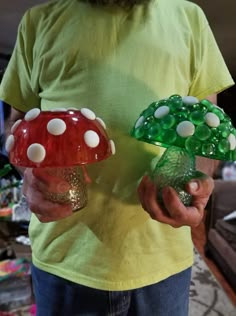 the man is holding two glass vases with mushrooms on them, both in different colors