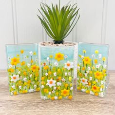 three square glass vases with flowers painted on them and a plant in the middle