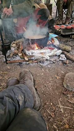 two men sitting around a campfire cooking food