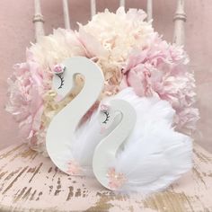 two white swans sitting on top of a wooden chair next to pink and white flowers