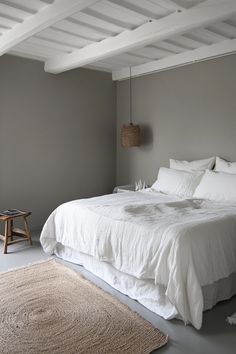 a white bed sitting in a bedroom on top of a wooden floor next to a rug