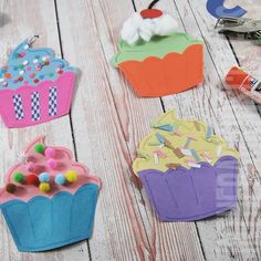 three cupcakes made out of construction paper on a white wooden table with scissors and glue