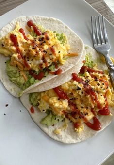 two breakfast tacos on a white plate with a fork and knife next to it