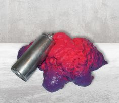 a red and purple substance next to a metal can on a white surface with grey background