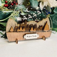 a wooden plaque with a christmas scene on it's front and back sides, sitting in front of some greenery