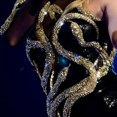 a woman in a black and gold dress on stage with her hands up to her chest