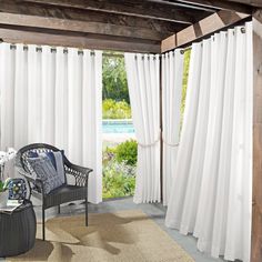 a living room with white curtains and a wicker chair in front of the sliding glass door