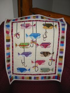 there is a fish quilt on the back of a chair with fishing hooks hanging from it