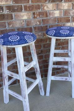 two wooden stools with blue and white designs on them next to a brick wall