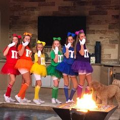 the girls are dressed in colorful outfits and holding up their hands while standing around a fire pit