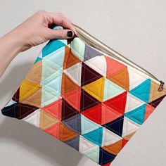 a hand holding a colorful patchwork purse on top of a white wall with a gold zipper