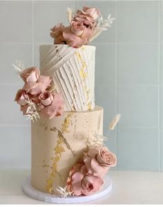 a three tiered cake with pink flowers on top and white icing, sitting on a table