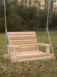 a wooden swing with chains hanging from it's sides in the grass near some trees