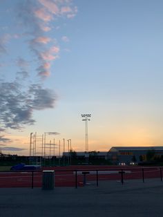 the sun is setting over an empty field with some clouds in the sky above it