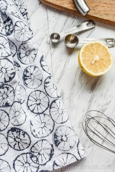 a cutting board, measuring spoons and an orange on a marble counter top with other kitchen utensils