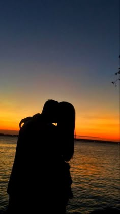 the silhouette of two people kissing in front of a body of water at sunset or dawn