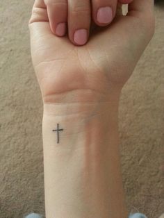 a woman's wrist with a small cross tattoo on the middle of her arm