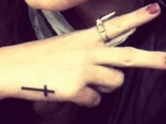 a person with a cross tattoo on their left hand pointing to the right side of her finger