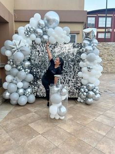 a woman standing in front of an arch made out of silver and white balloons with stars on it