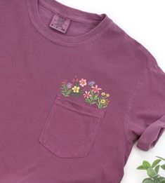 Comfort Colors Embroidered crewneck wildflower pocket tshirt. Embroidered flower shirt. Flower Boho Shirt. Gift for her or Girlfriend Gift. PLEASE NOTE THAT THE PICTURES ON THE LISTING ARE SAMPLES ONLY. If interested in adding embroidery to the sleeve please go to this listing: https://www.etsy.com/listing/1674502020 Because it is made to order, we don't accept the return or exchange unless we make a mistake We are unable to replace or refund purchases based on the color and the font selections. Cute Crew Neck Top With Pockets, Cheap Embroidered T-shirt For Spring, Casual Purple Tops With Embroidered Graphics, Purple Crew Neck Top With Floral Embroidery, Cute Floral Embroidery Crew Neck T-shirt, Cute Crew Neck T-shirt With Floral Embroidery, Green T-shirt With Floral Embroidery, Purple Floral Embroidered Crew Neck Top, Wildflower Pocket Shirt Embroidered