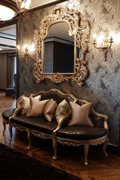 an ornate couch with pillows in front of a mirror and chandelier on the wall