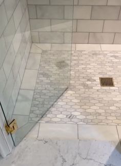 a shower with a glass door next to a white tiled wall and floor in a bathroom