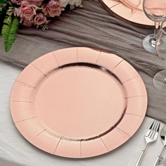 a pink plate sitting on top of a table next to wine glasses and silverware