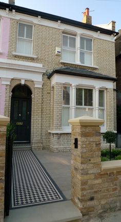 a brick house with white windows and black door on the side walk in front of it