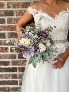 a woman in a wedding dress holding a bridal bouquet with purple and white flowers