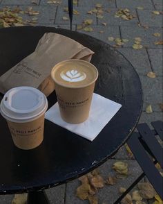 two cups of coffee sitting on top of a table next to a brown paper bag