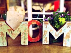 the word mom spelled out in wood letters on a table next to a potted plant