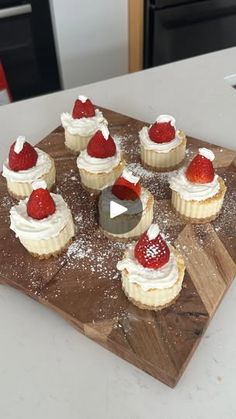 a wooden board topped with cupcakes covered in frosting and strawberries on top