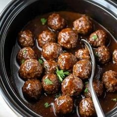 the meatballs are being cooked in the crock pot with a spoon and garnish