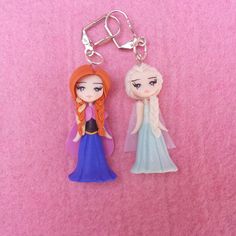 two frozen princesses keychains on a pink background, one is wearing a blue dress and the other has a red hair