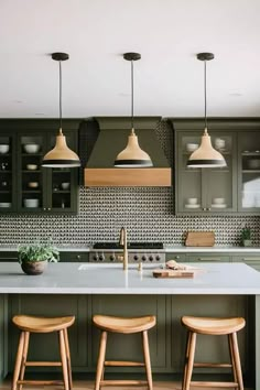 three stools sit in front of an island with two lights above it and green cabinets