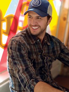 a man wearing a hat sitting at a table in front of a colorful wall with letters on it