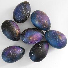 six black and purple painted eggs on a white surface with stars in the sky above them