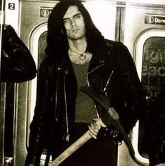 a man with long hair holding a large ax in his hand while standing next to a subway car