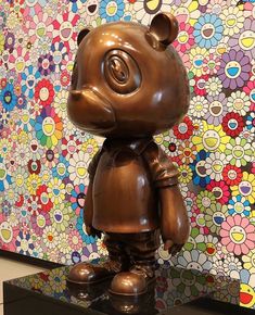 a brown bear statue sitting on top of a table next to a wall with flowers