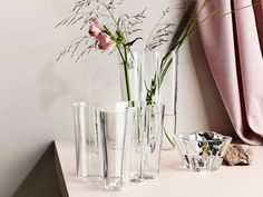 three clear vases with flowers in them on a table next to a pink curtain