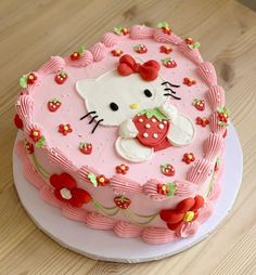 a pink hello kitty cake with flowers on the top and bottom, sitting on a wooden table