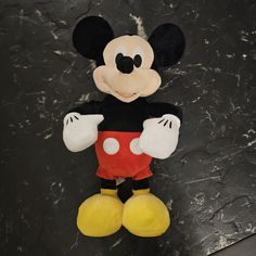 a mickey mouse stuffed animal sitting on top of a black table next to a wall